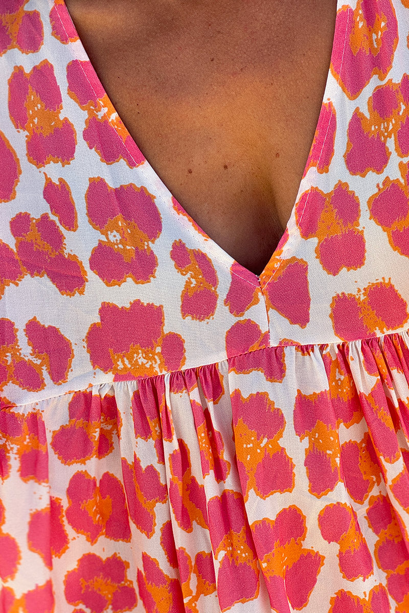 Vestido blanco largo fluido con estampado de leopardo rosa y naranja, escote en pico y mangas sueltas.