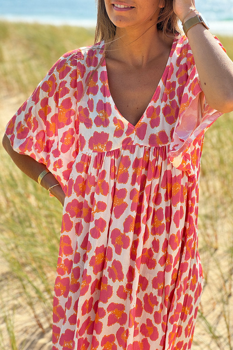 Vestido blanco largo fluido con estampado de leopardo rosa y naranja, escote en pico y mangas sueltas.