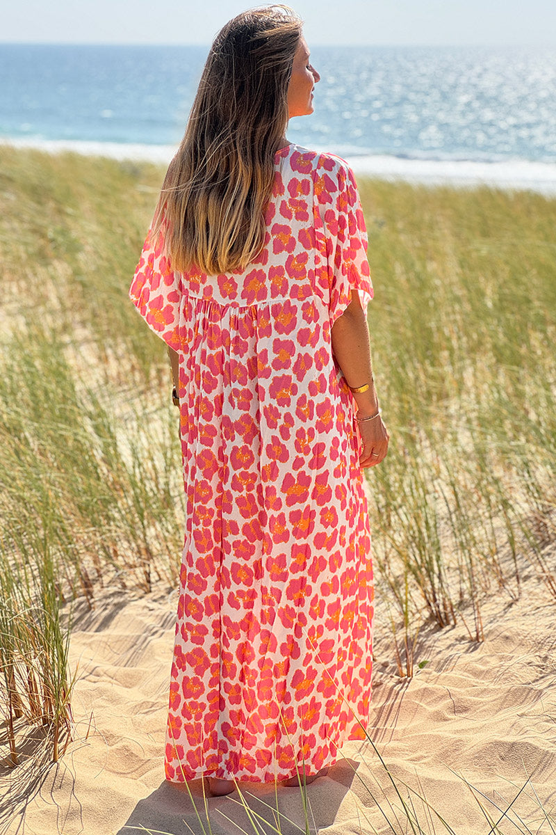 Vestido blanco largo fluido con estampado de leopardo rosa y naranja, escote en pico y mangas sueltas.