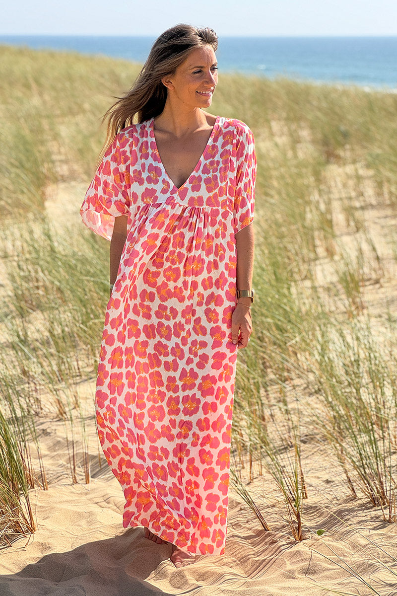 Vestido blanco largo fluido con estampado de leopardo rosa y naranja, escote en pico y mangas sueltas.